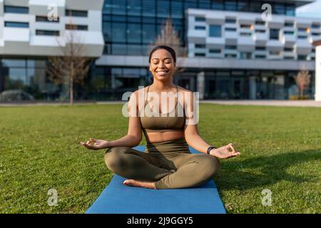 Femme noire millénaire en tenue de sport méditant sur le tapis de yoga dans le parc urbain, pleine longueur Banque D'Images