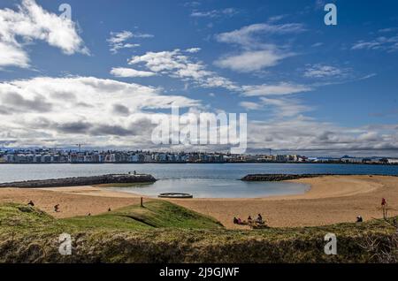 Reykjavik, Islande, 21 avril 2022 : plage de sable à Nautholsvik sous un ciel ensoleillé avec des quartiers de banlieue de l'autre côté de la baie Banque D'Images