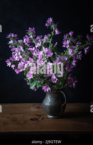 Malva sylvestris dans un vieux vase sur le fond sombre. Fleurs de malow commun (Malva sylvestris). Banque D'Images