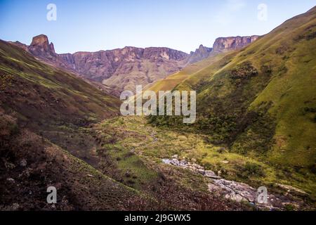 Une vieille femme coule à travers une gorge isolée dans les montagnes du Drakensberg en Afrique du Sud avec les falaises abruptes de basalte qui montent en arrière-plan. Banque D'Images