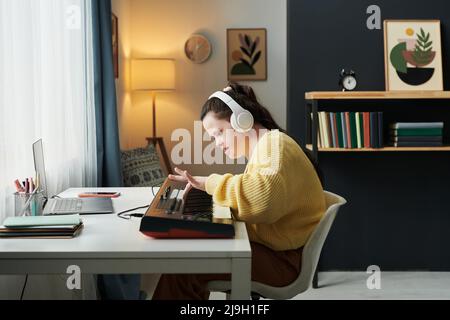 Vue latérale d'une jeune femme caucasienne atteinte du syndrome de Down, portant un casque, apprenant à jouer au clavier électronique Banque D'Images