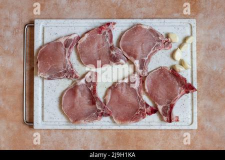 Vue en hauteur d'une longe de porc côtelettes sur une planche à découper sur un arrière-plan artistique abstrait en marbre avec de l'ail prêt à cuire. Recettes de viande. Banque D'Images