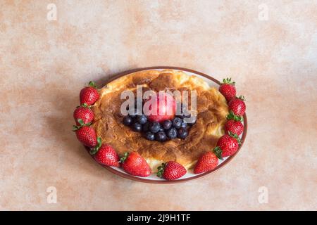 Assiette ronde avec délicieux cheesecake maison entourée de fraises avec prune rouge et bleuets au centre sur un fond pastel abstrait Banque D'Images