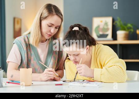 Professeur d'art professionnel ayant une classe individuelle avec une fille avec le syndrome de Down tableau avec aquarelles sur papier Banque D'Images