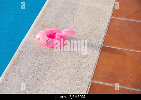 petit flotteur rose flamant dégonflé sur le bord d'une piscine Banque D'Images