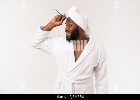 portrait d'un heureux jeune anm foncé se brossant les dents avec du dentifrice noir sur fond blanc. Banque D'Images