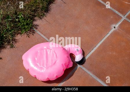 petit flotteur rose flamant dégonflé sur le bord d'une piscine Banque D'Images