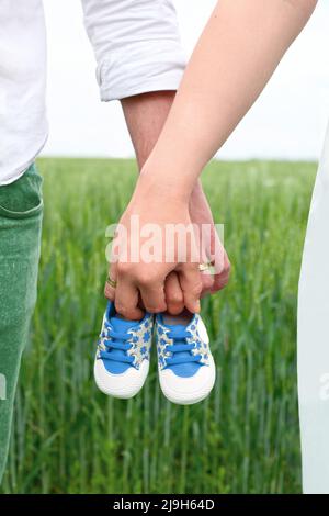 Attente de bébé. C'est un garçon! Une femme et un homme tiennent des chaussures pour enfants dans la prairie à l'extérieur. Je m'attends à un bébé garçon. Banque D'Images