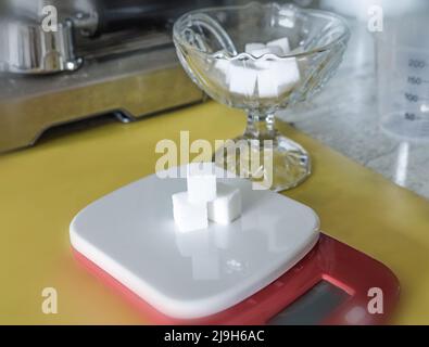 Cubes de sucre sur une balance électronique, dans la cuisine. Une tasse en cristal. Banque D'Images