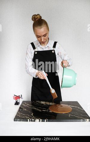 Gros plan photo - une femme agite du chocolat et des fours sur un plateau en pierre pour faire des chocolats faits maison. Fabrication de bonbons, production de pâtisseries, concept de dessert Banque D'Images