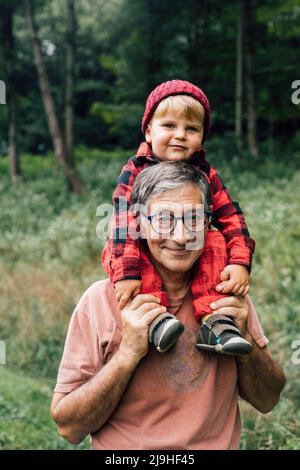 Homme senior souriant portant petit-fils sur les épaules Banque D'Images