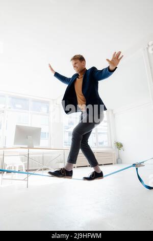 Homme d'affaires souriant aux bras tendus sur la corde raide au bureau Banque D'Images