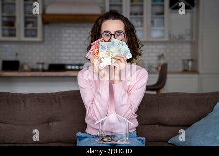 Jeune femme qui couvre la bouche avec des devises de papier à la maison Banque D'Images
