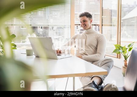 Smiling young businessman using laptop at desk in office Banque D'Images