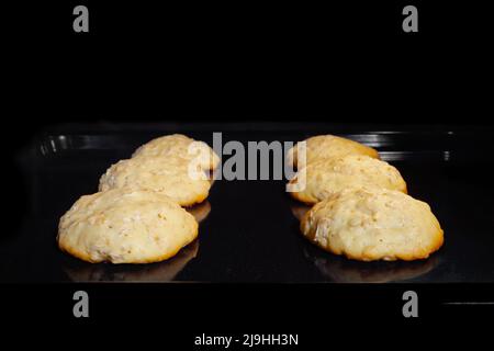 Cuisson de six biscuits aux flocons d'avoine croquants sur une tôle métallique dans le four - vue de face Banque D'Images