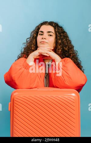 Jeune femme avec les mains classed pendu sur la valise orange sur fond bleu Banque D'Images