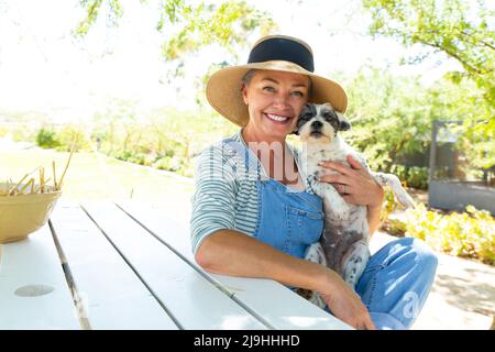 Femme souriante avec un chien assis à une table dans le jardin Banque D'Images