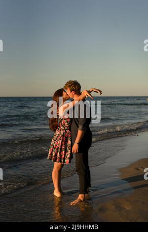 Un jeune couple affectueux s'embrasse à la plage au coucher du soleil Banque D'Images