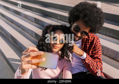 Couple souriant prenant le selfie à travers le smartphone sur les marches Banque D'Images