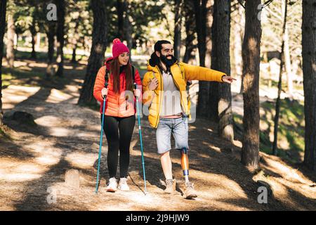 Heureux homme handicapé pointant vers l'extérieur par une femme marchant avec le poteau de randonnée dans la forêt Banque D'Images