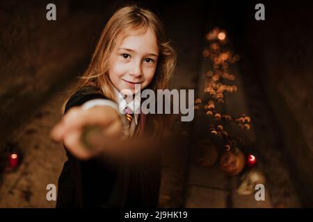 Fille blonde avec baguette magique portant un costume de sorcière debout dans un tunnel effrayant Banque D'Images