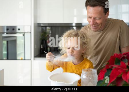 Homme souriant regardant la fille soufflant de la farine dans la cuisine Banque D'Images