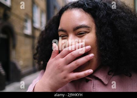 Jeune femme gaie riant avec la main couvrant la bouche Banque D'Images