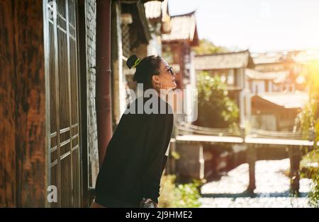 femme asiatique se détendant et profitant de la lumière du soleil à l'extérieur d'une maison traditionnelle en bois Banque D'Images