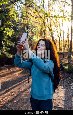 Femme utilisant un smartphone avec des icônes augmentées en forêt Banque D'Images