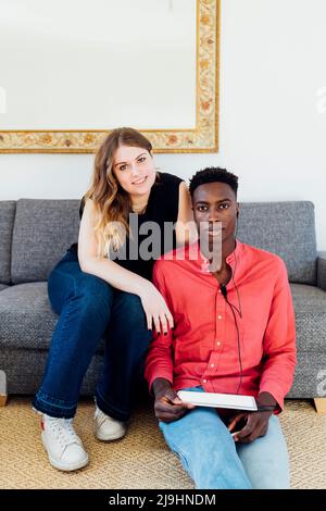 Jeune homme avec une tablette PC numérique assis par une petite amie dans le salon à la maison Banque D'Images