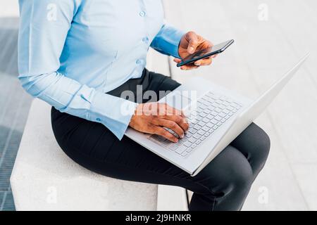 Femme d'affaires utilisant un téléphone portable assis avec un ordinateur portable sur un bloc de béton Banque D'Images