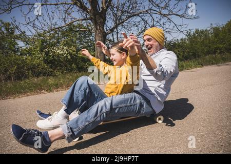 Homme senior joyeux qui profite du skateboard avec sa petite-fille sur la route Banque D'Images