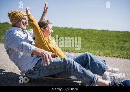 Homme senior joueur qui apprécie le skateboard avec sa petite-fille sur la route Banque D'Images