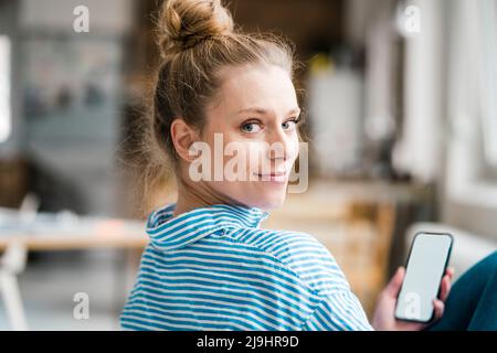 Un travailleur indépendant souriant qui regarde par-dessus l'épaule tout en tenant un smartphone Banque D'Images
