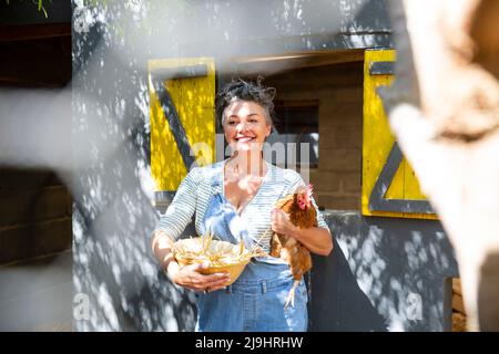Joyeux fermier avec un bol de poule et d'œuf debout devant le coop de poulet Banque D'Images
