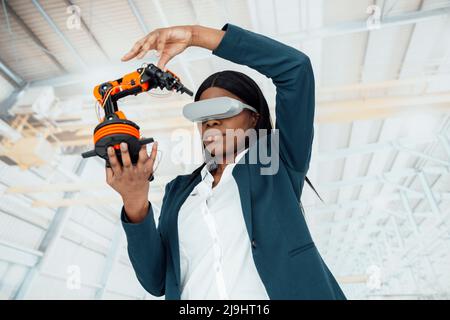 Ingénieur portant un simulateur de réalité virtuelle tenant le modèle de bras robotique en usine Banque D'Images
