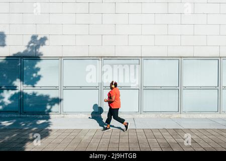 Femme écoutant de la musique avec un casque sans fil qui fait du jogging sur la piste de marche Banque D'Images