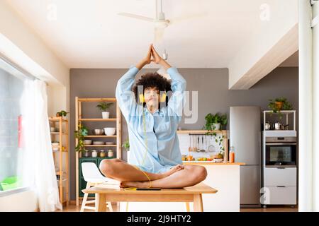 Jeune femme portant un casque méditant sur la table à manger à la maison Banque D'Images