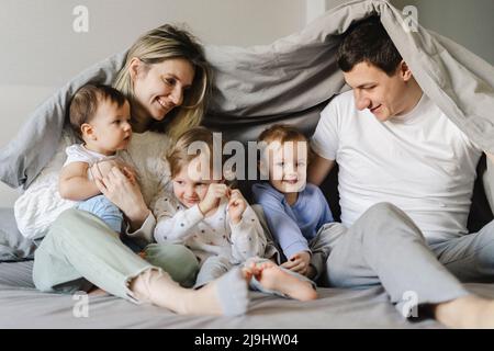 Parents heureux avec enfants assis sous une couverture dans la chambre Banque D'Images