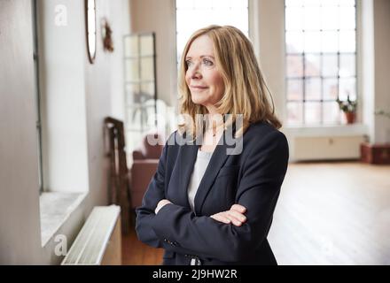 Femme d'affaires souriante portant un blazer debout avec les bras croisés à la maison Banque D'Images