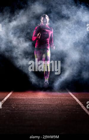 Une jeune femme qui fait du jogging la nuit sur une piste de course au milieu du brouillard Banque D'Images