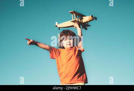 Pilote enfant montrant ou pointant l'espace de copie. Petit garçon avec avion en bois. Garçon avec un avion en plein air, fond de ciel. Banque D'Images