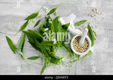 Studio de mortier et de pilon, de pignons et de feuilles de ramson fraîches reposant sur une surface en bois Banque D'Images