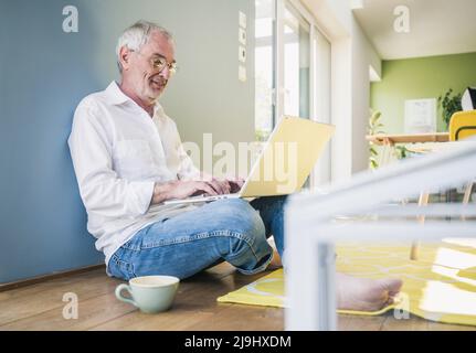 Homme senior souriant portant des lunettes à l'aide d'un ordinateur portable à la maison Banque D'Images