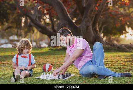 Fils se posant sur l'herbe et jouant aux échecs avec le père. École d'échecs pour enfants. Banque D'Images