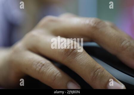 Une photo montre que la main tient la souris sur la table avec un arrière-plan flou Banque D'Images