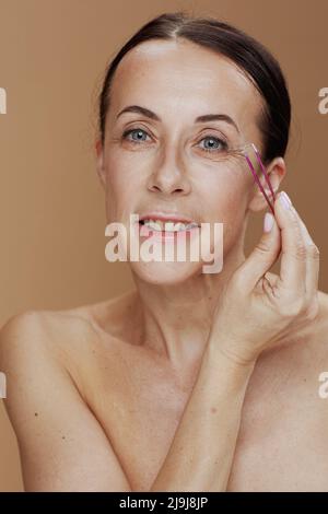 Portrait d'une femme moderne avec pince à épiler sur fond beige. Banque D'Images