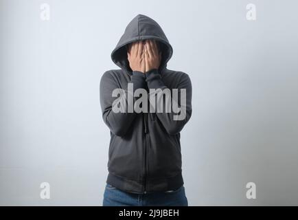 portrait d'un homme à capuchon couvrant son visage à l'aide des mains Banque D'Images