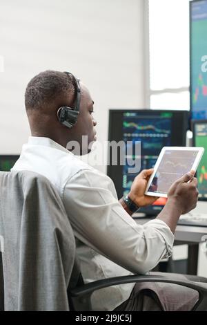 Homme afro-américain tenant une tablette numérique travaillant avec des statistiques boursières observant des graphiques et des graphiques de monnaie Banque D'Images