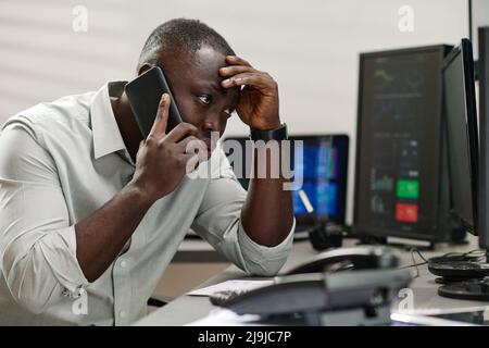 Jeune homme noir travaillant avec dans l'industrie de la bourse se sentant stressé de parler à un client insatisfait Banque D'Images